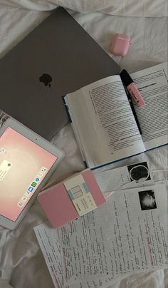 an open laptop computer sitting on top of a bed next to books and papers with writing