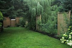 a lush green yard with lots of trees and flowers on the grass, next to a wooden fence