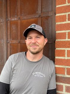 a man standing next to a brick wall wearing a gray shirt and black baseball hat