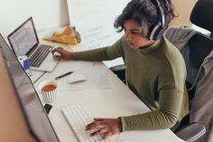 a woman wearing headphones working on her computer at the desk with a cup of coffee in front of her