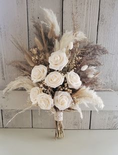 a bouquet of white roses sitting on top of a table next to some brown feathers