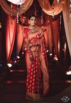 a woman in a red and gold sari standing under an archway with lights on either side