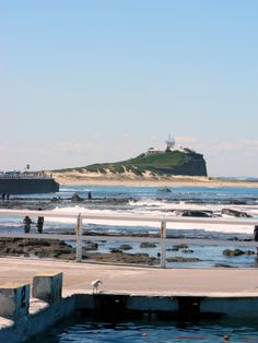 people are standing on the pier near the water and an island in the distance,