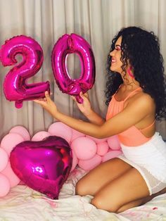 a woman sitting on top of a bed with balloons in front of her and the number 20