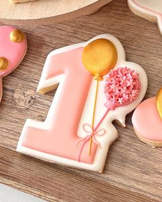 decorated cookies with pink and gold decorations on a wooden table, including one for the first birthday