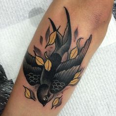 a black bird with yellow leaves on it's wings is sitting on the arm