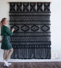 a woman is standing in front of a wall hanging with fringes and an arrow