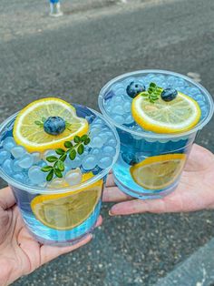 two cups with lemon slices and blueberries in them are being held by someone's hand