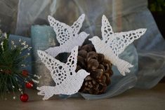 two white crocheted christmas decorations with pine cones