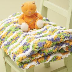 an orange teddy bear sitting on top of a blanket that is laying on a chair