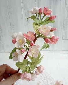 a hand holding a piece of paper with pink flowers on it and green leaves in the middle