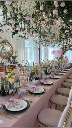 a long table is set with pink and white flowers on the ceiling, plates and silverware