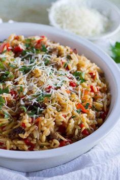 a white bowl filled with pasta and vegetables on top of a table next to some parmesan cheese