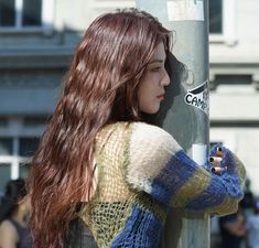 a woman leaning against a pole with her hand on the pole and looking at something