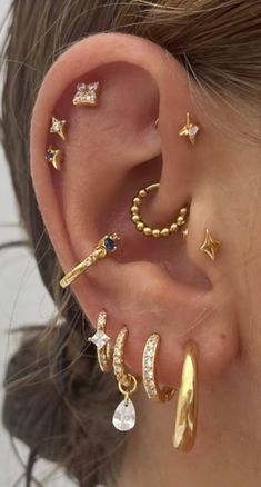 a woman wearing gold ear piercings with stars and moon designs on the side of her ear