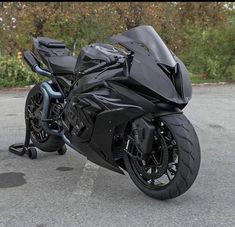 a black motorcycle parked in a parking lot next to some bushes and trees on the other side