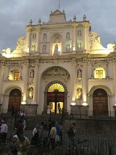 people are standing in front of an ornate building at night with lights on the doors and windows