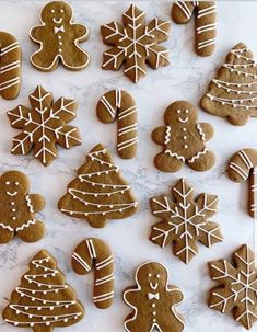 gingerbread cookies decorated with icing on a white marble counter top, surrounded by christmas trees and snowflakes