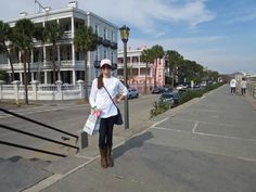 a woman is standing on the sidewalk with her hand in her pocket and holding shopping bags