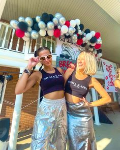 two women standing next to each other in front of a building with balloons on the roof