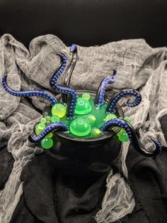 an octopus is sitting in a black bowl with green and blue beads on it's legs