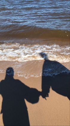 the shadow of two people holding hands at the beach with waves coming in behind them