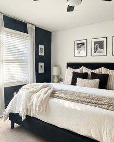 a white and black bedroom with pictures on the wall above the bed, along with two windows