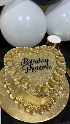 a birthday cake sitting on top of a gold plate next to balloons and streamers