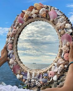 a person holding up a mirror made out of seashells