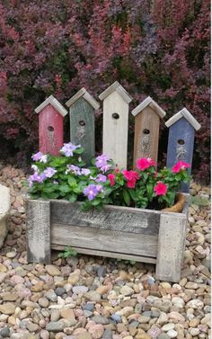 several birdhouses and flowers in a wooden planter filled with rocks on the ground