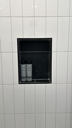 two bottles are sitting in the corner of a white tiled shower stall with black grouting