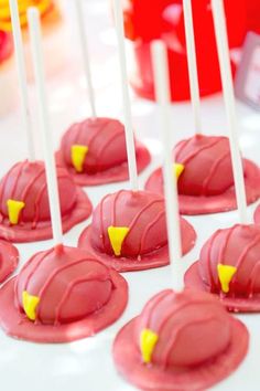 red cake pops with yellow candies on them sitting on a white tablecloth covered table