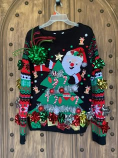 an ugly christmas sweater hanging on a wooden door with ornaments and decorations around the tree