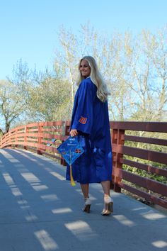 a woman walking across a bridge wearing a blue graduation gown and holding a book in her hand