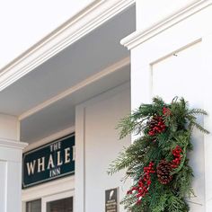 a wreath hanging on the side of a white building with red berries and pine cones