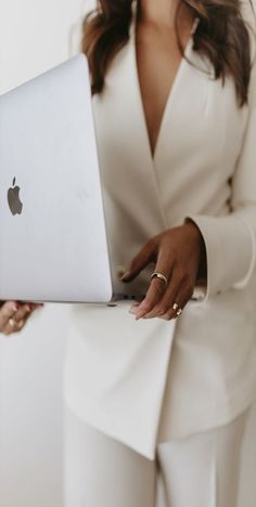 a woman holding an apple laptop computer in her right hand and wearing a white suit