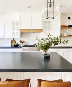 a kitchen with white cabinets and black counter tops, two brown chairs in front of the island