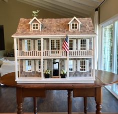 a doll house sitting on top of a wooden table next to a flag and window