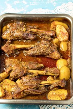 a pan filled with meat and potatoes on top of a blue table cloth next to a knife