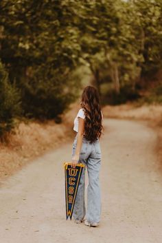 a girl holding a pennant on a dirt road in front of some trees and bushes