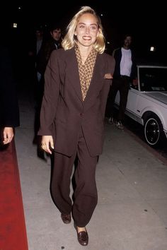 a woman in a suit and tie walking down the street at night with other people behind her