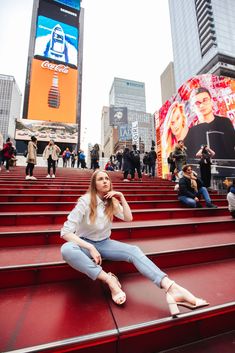 a woman is sitting on the steps in front of some tall buildings and billboards