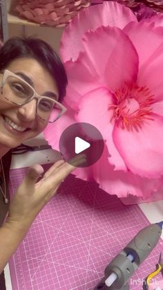 a woman is cutting paper with scissors and a large pink flower in front of her