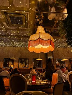 people sitting at tables in a restaurant with lights hanging from the ceiling