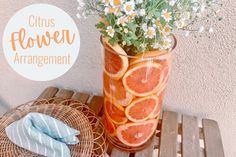 a vase filled with orange slices and flowers on top of a wooden table next to a wicker basket