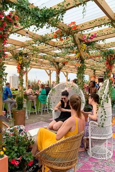 people sitting in chairs under an open roof with flowers on the ground and plants growing all over them