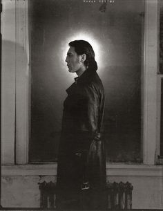 black and white photograph of a woman standing in front of a window wearing a leather coat