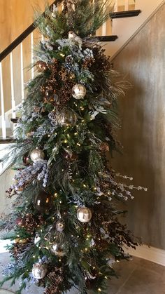 a christmas tree with ornaments and lights on the bottom is in front of a stair case