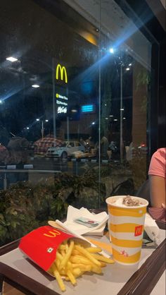 a tray with french fries and a drink sitting on a table in front of a mcdonald's window