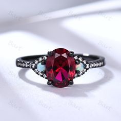 a ring with a red stone surrounded by white and black diamonds on a white surface